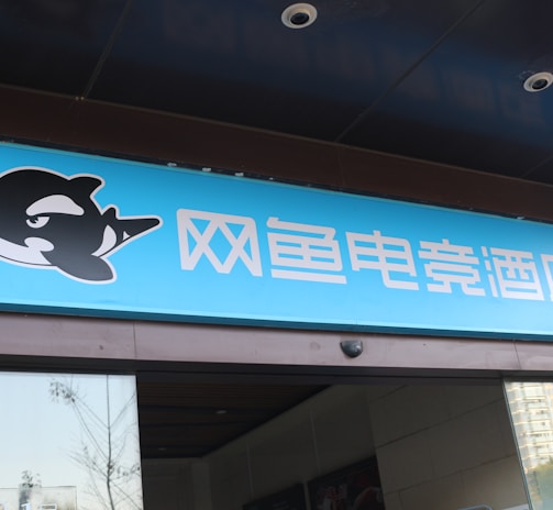 A building entrance features a vibrant blue sign with white Chinese characters and a stylized orca logo in black and white. The overall appearance suggests an establishment focused on eSports or digital activities.